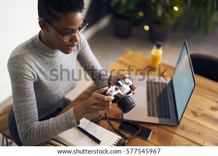 Young female international student testing usability of vintage camera enjoying taking photos spending free time on hobby while making homework sitting in university campus using free wifi connection