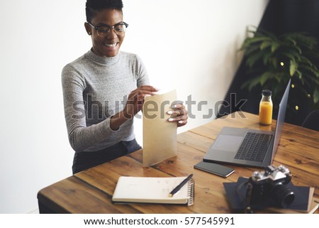 Portrait of smiling creative female photographer finishing working on image editing sending pictures to clients while sitting in modern studio using modern technologies and 5G wireless internet 