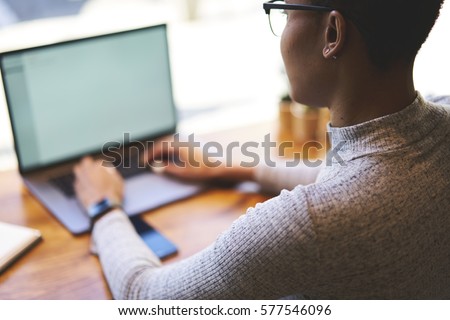Back view of female author typing text of her article for column in online newspaper via modern laptop computer with mock up screen connected to free wireless internet sitting in coworking space