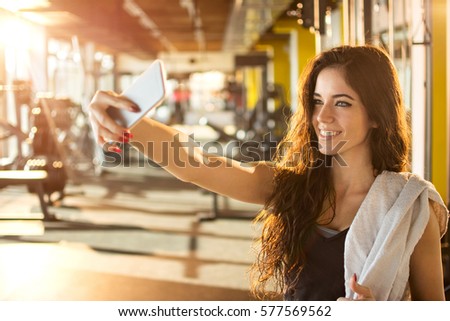 Young sporty woman taking a selfie with mobile phone for social networks at gym.