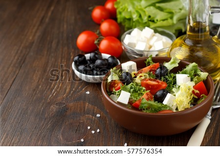 Tasty greek salad with feta, olives and tomatoes in a bowl on wooden background. Copy space for text.