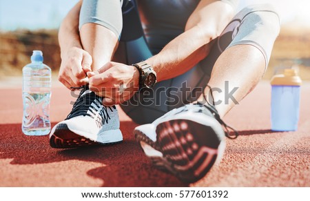 Tying sports shoe. A young sportsman getting ready for athletic and fitness training outdoors. Sport, exercise, fitness, workout. Healthy lifestyle  Royalty-Free Stock Photo #577601392