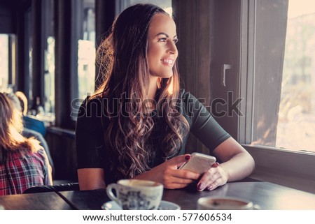 Smiling brunette woman using a smart phone in a cafe.