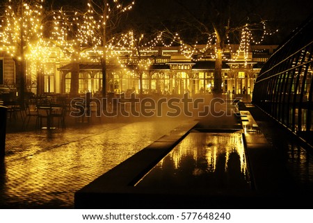 empty night restaurant, lot of tables and chairs with noone, magic fairy lights on trees like christmas celebration