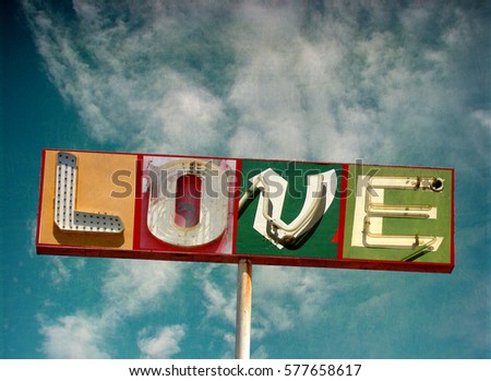 aged and worn vintage photo of neon love sign with cloudy sky
