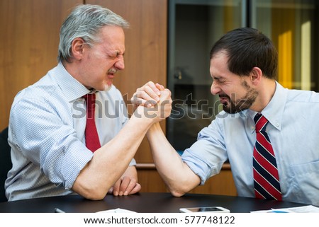 Business people doing arm wrestling in their office. Shallow depth of field, focus on the man on the right