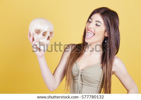 Young woman making fun with a skull, laughing at it. In studio, over a yellow background.