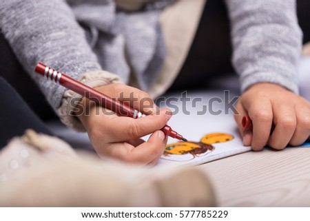 Artistic little girl making a colorful drawing on a sheet of paper with a colored pen in a close up view of her hands and artwork