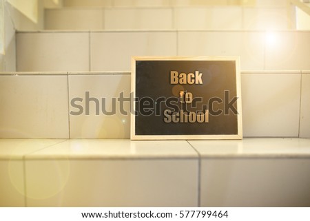 Black board on stairs with message "back to school ". Lenses flare effect applied