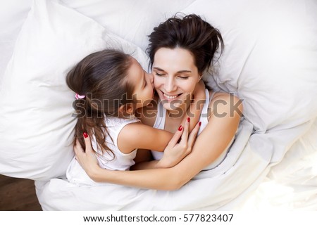 little daughter kissing her mother in bed