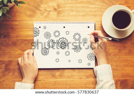 Gears with a person holding a pen on a wooden desk