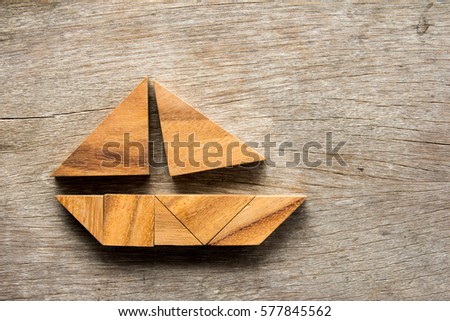Tangram puzzle in sail boat shape on wooden background