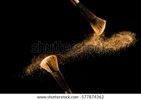 Cosmetic brush with golden cosmetic powder spreading on black background