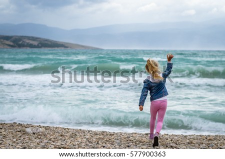 little lovely blond girl throwing stones into the heavy sea