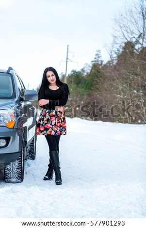 portrait of a beautiful young girl on a background of a winter pine forests and off-road vehicle on a country road