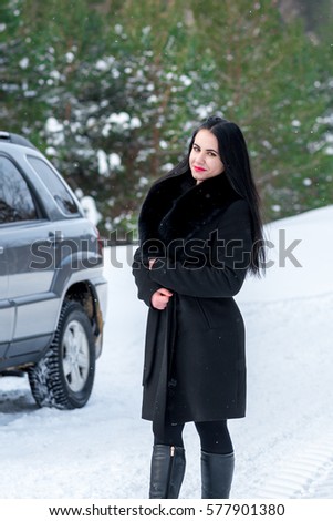portrait of a beautiful young girl on a background of a winter pine forests and off-road vehicle on a country road