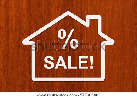 Paper house with SALE text inside on wooden background. Abstract conceptual image