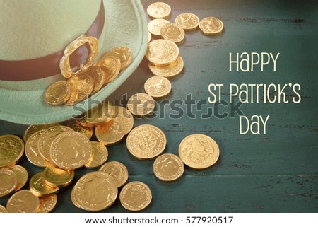 Happy St Patricks Day leprechaun hat with gold chocolate coins on vintage style green wood background with text and applied retro style faded filters.