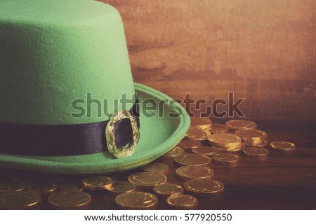 Happy St Patricks Day green leprechaun hat with gold covered chocolate coins on dark wood background, with applied retro style faded filters.