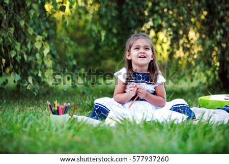Little girl drawing with colored pencils lying on the grass in the park