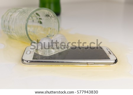 Beer in glass spilled smart phone on white table
