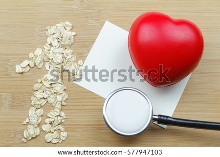 Oat grains to form a human shape with a blank paper, a heart shape and a stethoscope on wooden background. Concept of health.