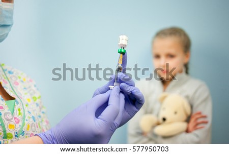 The pediatrician or nurse in a syringe vaccine, a girl in the background with the toy, the child vaccination