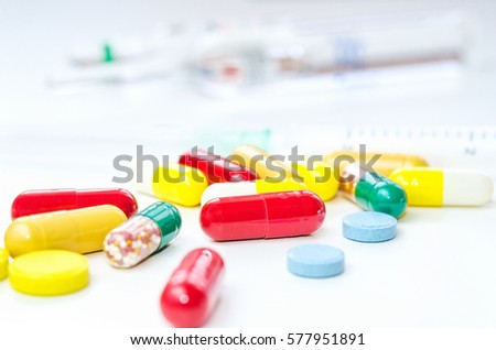 Colorful medicine pills, drugs and capsules with syringe and ampule on a white background. Selective focus. Close-up macro shot.