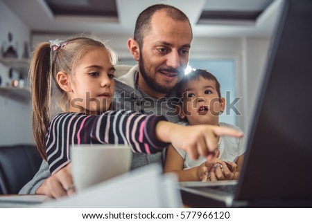 Father with two children watching cartoons on laptop at home office