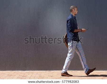 Profile portrait of black male student walking with tablet 