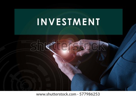 a business man touching a smart phone screen with flare on black background with text INVESTMENT