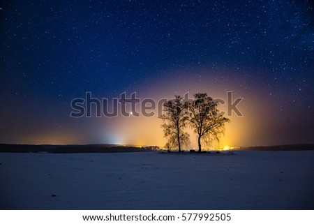 Milky way and starry sky over winter landscape and distant village. Night sky astrophotography background.