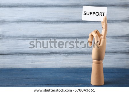 Mannequin hand holding white paper with word SUPPORT on wooden background
