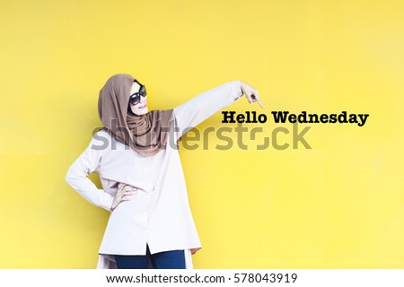 Asian young lady pointing her finger to the words typed Hellow Wednesday isolated with yellow background. Conceptual image for business, finance, inspiration and creativity.