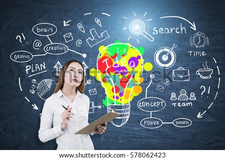 Portrait of an Asian businesswoman holding a clipboard and a pen and standing near a blackboard with a colorful creative idea sketch. Toned image