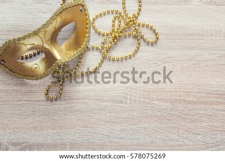 Golden masks and beads on a wooden background. Copy space for text.