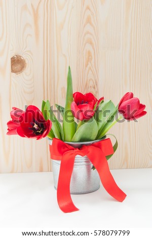 Bouquet of red tulips in a tin bucket with a red bow on a wooden background