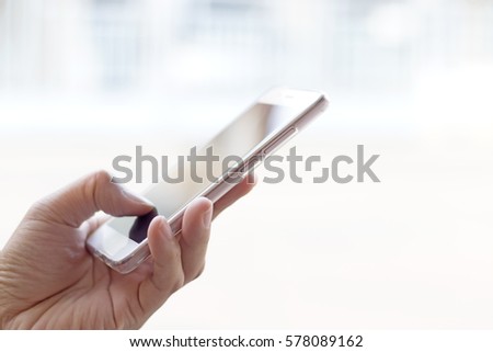 Hand holding mobile phone with white screen on white clear background.