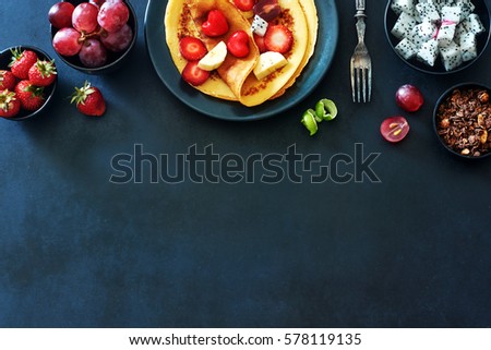 Gourmet breakfast with thin pancakes (crepes) with grapes, strawberries, golden kiwi, dragon fruit over dark background with a copy space.