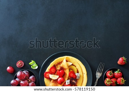 Top view of homemade crepes with strawberries, grapes and honey over black background with a copy space. 