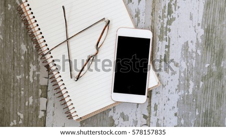 Mobile phone on notepad with glasses from above lay flat image