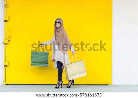 The Malaysian lady holding a Shopping Bag with authentatic smile and isolated with yellow and white background.
