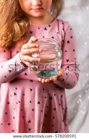 Baby girl in pink dress holding a aquarium with blue fish. The concept of care for Pets. Gift. Selective focus