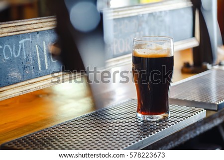 Nonic pint glass with dark stout ale standing on a pub counter near draft taps Royalty-Free Stock Photo #578223673