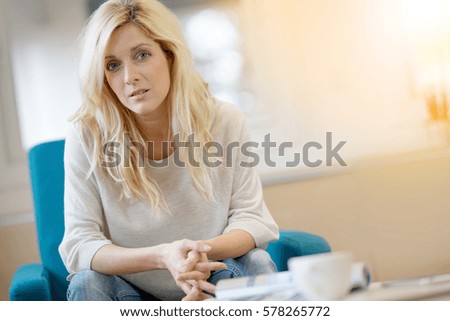 Woman with long blond hair sitting in armchair at home