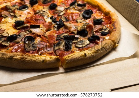 pizza with pepperoni, olives, bacon, mushroom, cheese in the pizza box (corrugated cardboard) on the wooden background