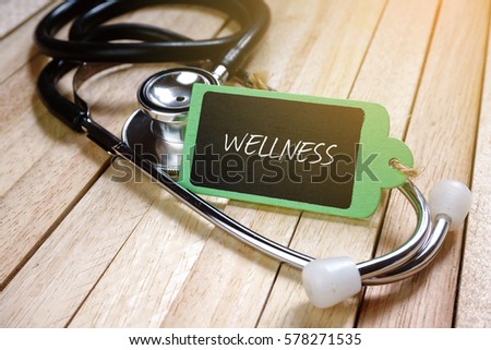 Stethoscope and wooden tag written with WELLNESS on wooden background. 
