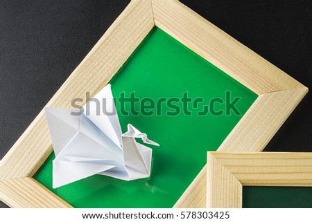Origami in wood, green frame and decorative stones nearby. Paper Swan.