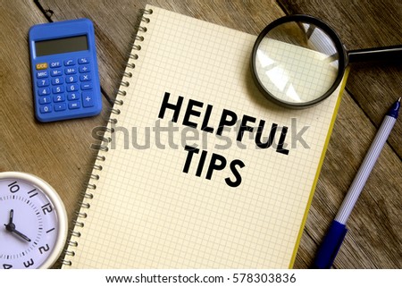 Business concept. Top view of table clock, calculator, magnifier, pen and notebook written HELPFUL TIPS on wooden background.