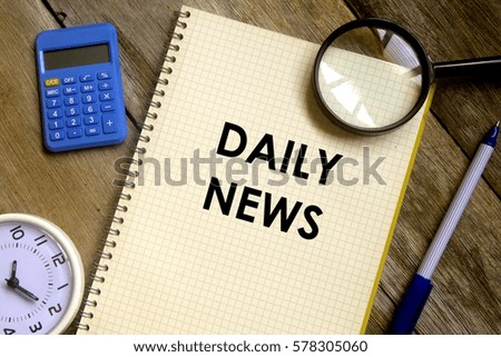 Business concept. Top view of table clock, calculator, magnifier, pen and notebook written DAILY NEWS on wooden background.